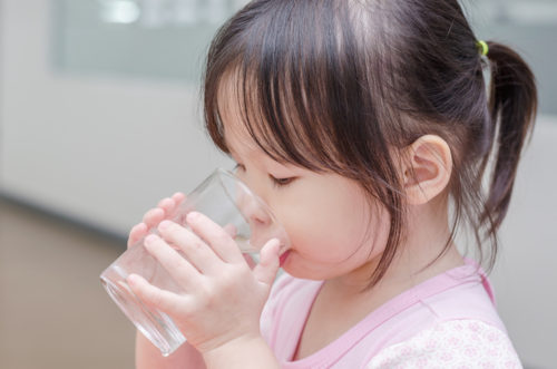 Little Asian girl drinking water from glass by herself