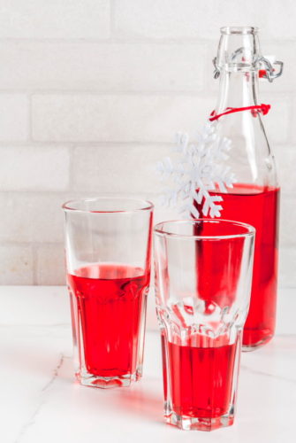Autumn, winter drinks. Homemade cranberry juice, in a bottle and glasses on white marble table. copy space