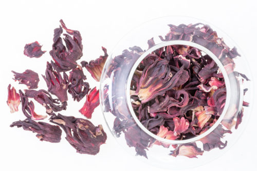 Overhead view of dried hibiscus tea leaves served in a glass bowl against a white background
