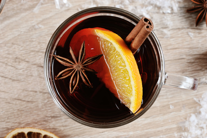 Mulled wine in a glass. A glass of drink is decorated with a cinnamon stick, a slice of lemon and anise. Light wooden background. Close-up. View from above.