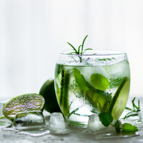 Homemade lime lemonade with cucumber, rosemary and ice, white background. Cold beverage for hot summer day. Copyspace.