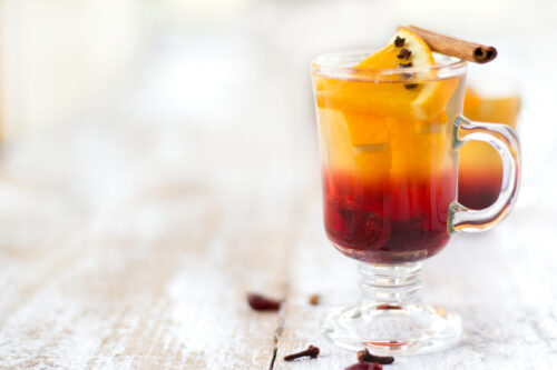 Delicious tea with cranberries, orange, cloves and cinnamon. On white, wood background.